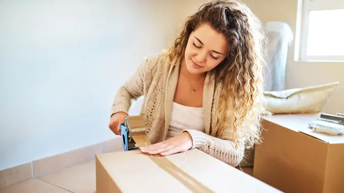Shot of a young woman sealing a box while moving house.