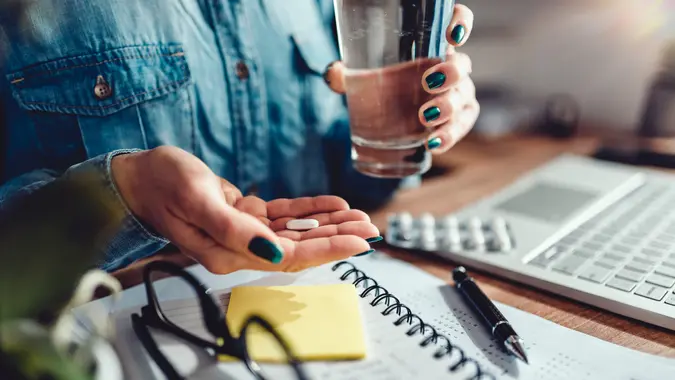 Woman wearing denim shirt sitting by the desk in the office and taking medical pills.