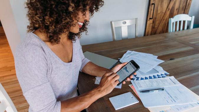 A woman sits at her dining room table with laptop and financial reports doing her monthly budget.