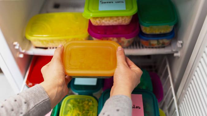 Woman placing container with frozen vegetables in freezer.