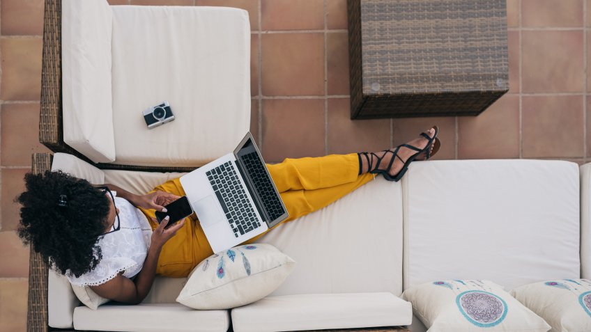 Woman working from home at the yard on her computer and typing on the mobile phone.
