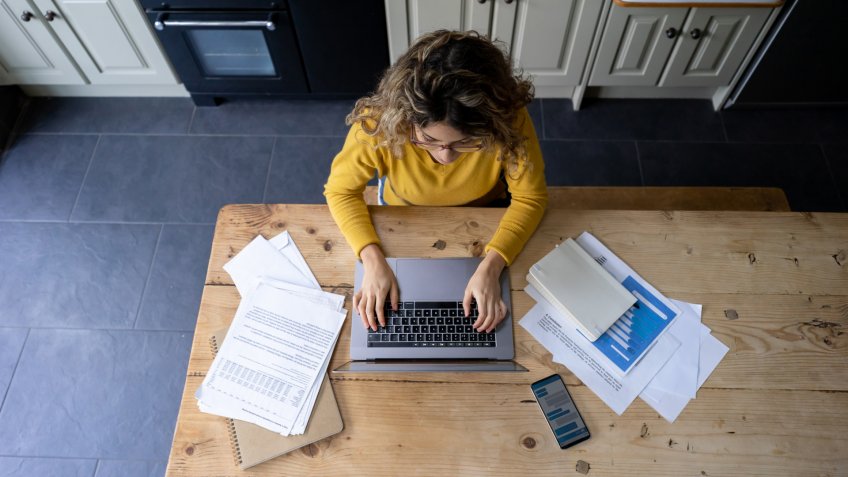 Woman working from home using paperwork and laptop.