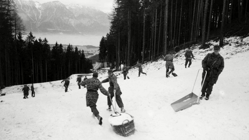 Austrian soldiers use baskets to haul snow down to part of the downhill slope that will be used for the Bobsled run in the IX Winter Olympic Games, in Innsbruck, Austria on .