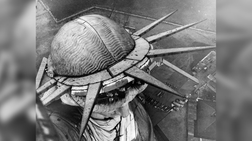 A group of people leaning out of the head of the Statue of Liberty in New York, seen from the torch above.