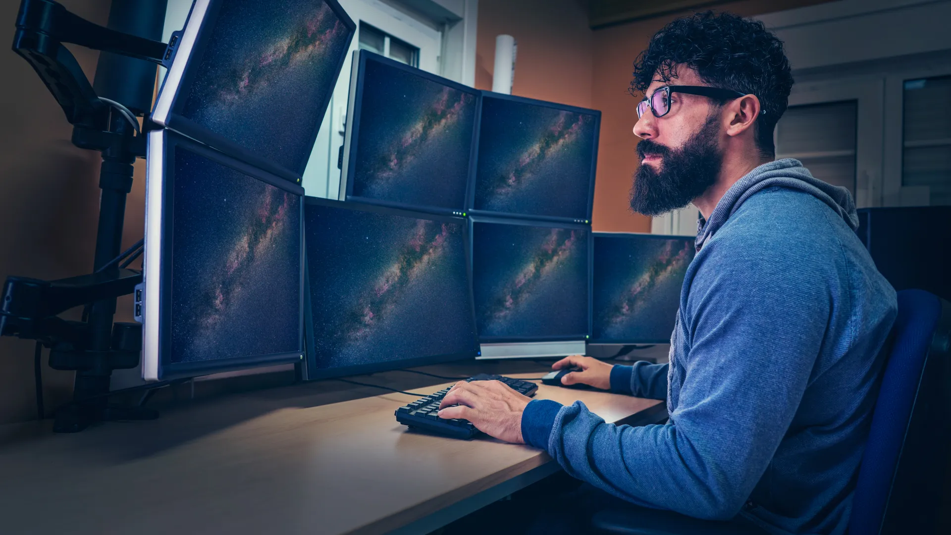 Astronomer in control panel room multi screen sitting profile with beard.