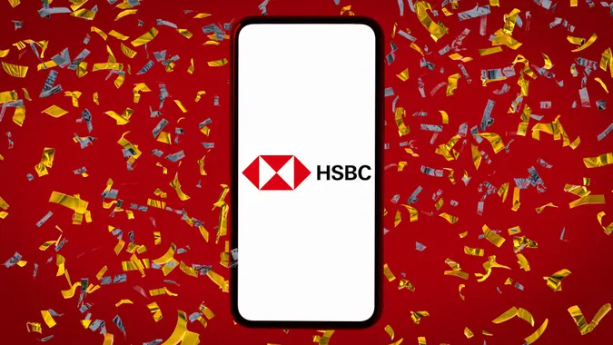 HSBC Bank logo displayed on a phone screen, set against a vibrant red background with blue and gold confetti accents.