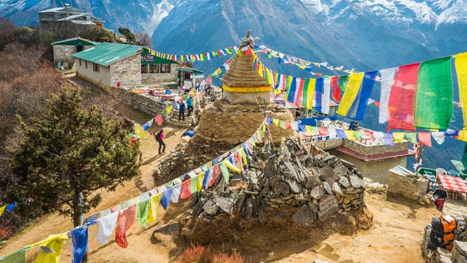 Namche Bazaar, Nepal - November 2, 2014: Hikers trekking past a traditional stupa shrine festooned with colourful Buddhist prayer flags fluttering in the breeze above a collection of Sherpa teahouses and lodges deep in the Himalayan mountains of the Everest National Park, a UNESCO World Heritage Site, Nepal.