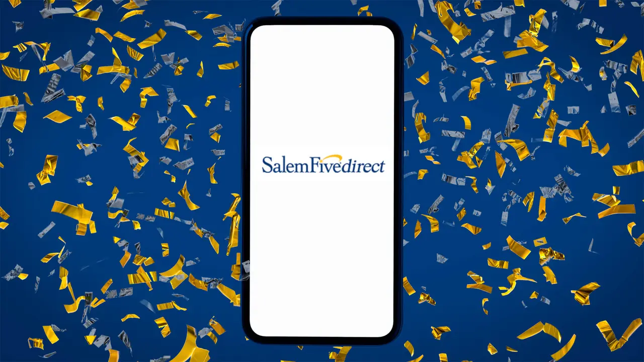 Phone displaying the Salem Five Direct logo on the screen lays on top of a background of blue and yellow confetti