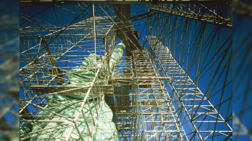 Statue of Liberty during restoration, looking straight up torch arm showing scaffolding and draped robe, Liberty Island, New York City, c.