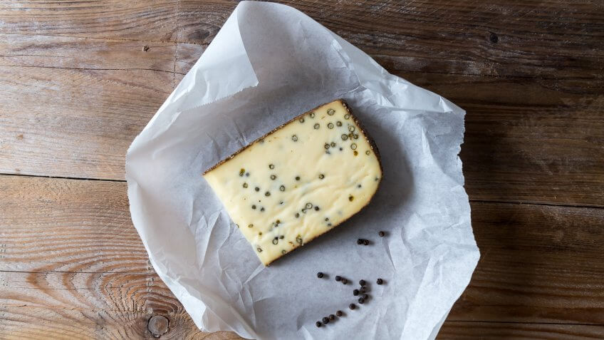 Pepper cheese and peppercorns on a wooden table.