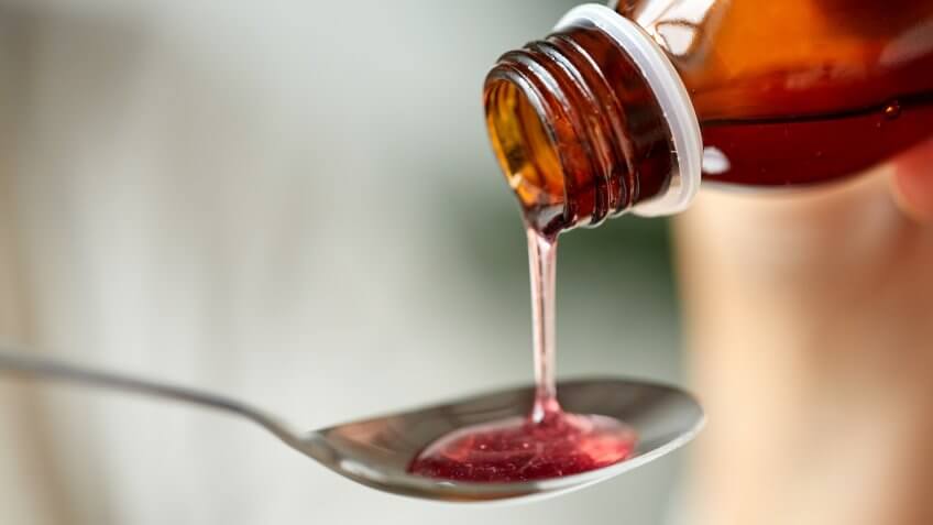 healthcare, treatment and medicine concept - bottle of medication or antipyretic syrup and spoon.