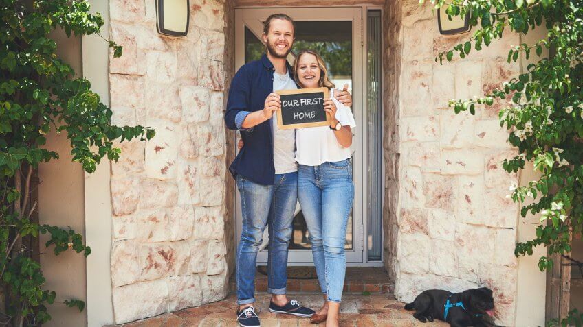 Portrait of a young couple holding a chalkboard with "our first home" written on it.