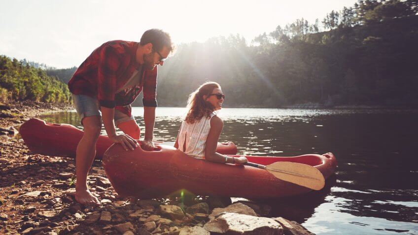 Young man pushes a canoe in the water while a woman sitting on the canoe.