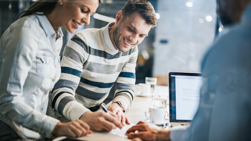 Young happy couple signing a document while being on a meeting with their real estate agent in the office.