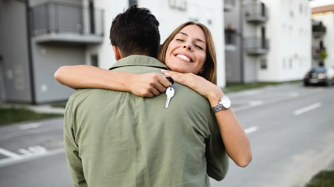 Happy young couple with key standing outside in front of their new home.