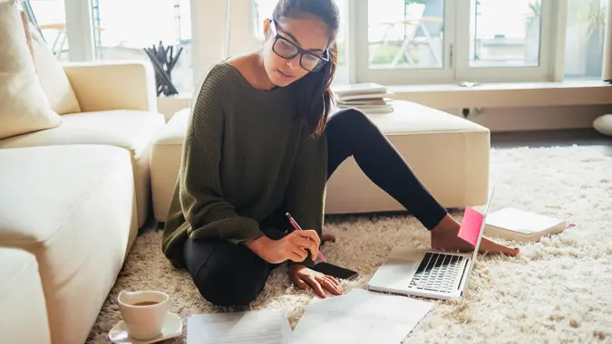 young woman studying in her living room,sitting on the carpet.