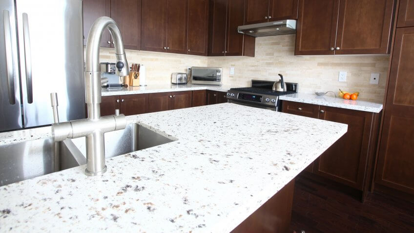 Modern kitchen with stainless steel appliances, limestone backsplash, quartz counter tops, chestnut color cabinetry, small appliances and goose-neck brushed nickel faucet.