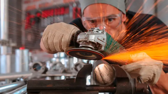 man work in home workshop garage with angle grinder, goggles and construction gloves, sanding metal makes sparks closeup, diy and craft concept.