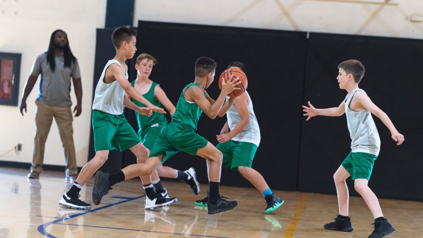 A young African American boy dribbles around three defenders and tries to score.
