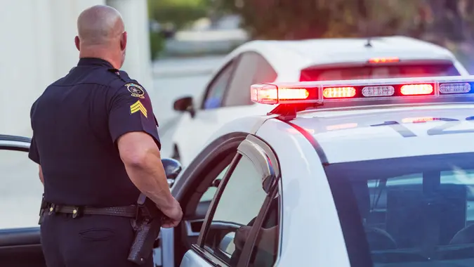 Policeman pulls over a driver for speeding, getting out of police car to write a traffic ticket.