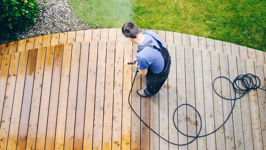 cleaning terrace with a power washer - high water pressure cleaner on wooden terrace surface.