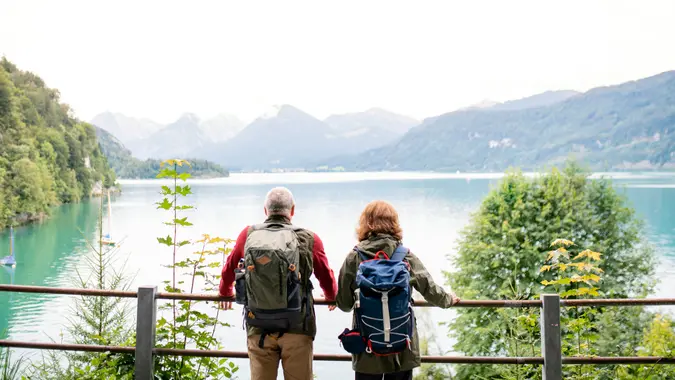 A rear view of senior pensioner couple standing by lake in nature.