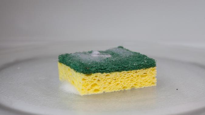 A green and yellow sponge covered in soap suds sits inside of a microwave.