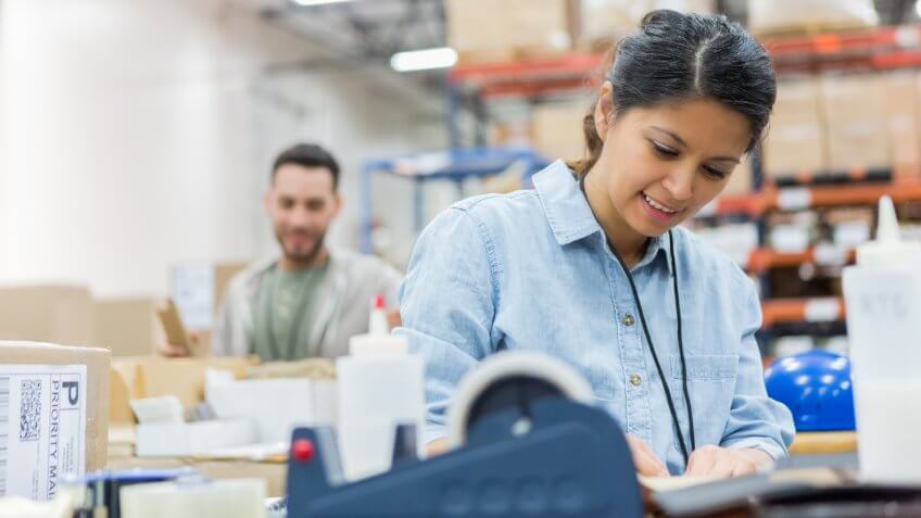 Confident mid adult distribution warehouse employee concentrates while preparing a package for delivery.