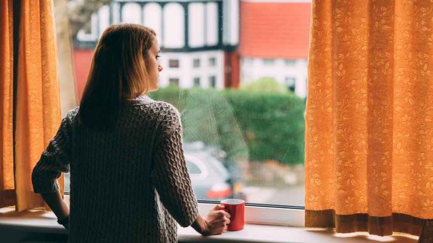 Woman staying home for safety during coronavirus pandemic and observing empty city.