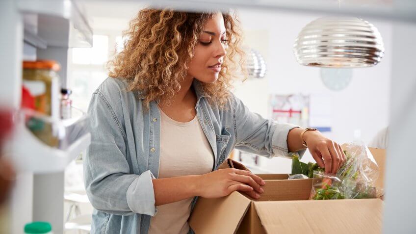 View Looking Out From Inside Of Refrigerator As Woman Unpacks Online Home Food Delivery.
