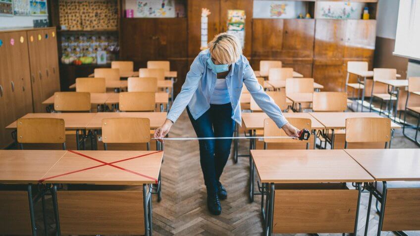 Teacher measuring and marking places in the classroom for returning of students after the coronavirus pandemic.