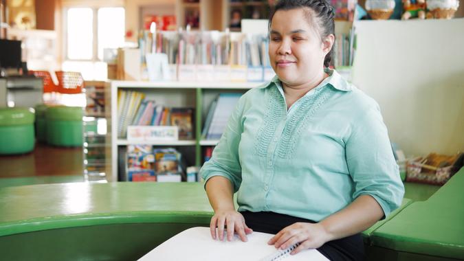 Portrait of Asian young blind woman disabled person reading Braille book in creative workplace.