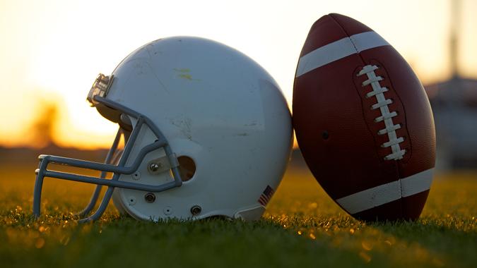 American Football and Helmet on the Field Backlit at Sunset.