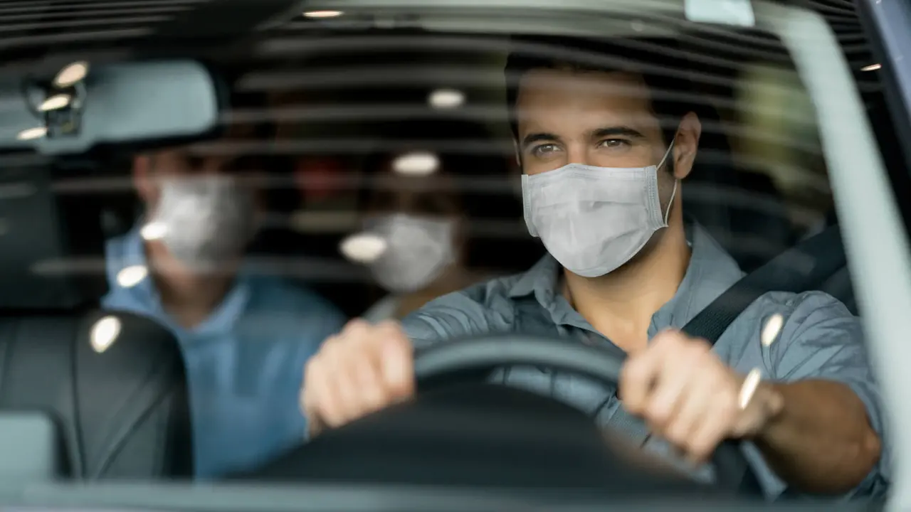Portrait of a crowdsource taxi driver wearing a facemask while driving a couple of customers during the COVID-19 pandemic.