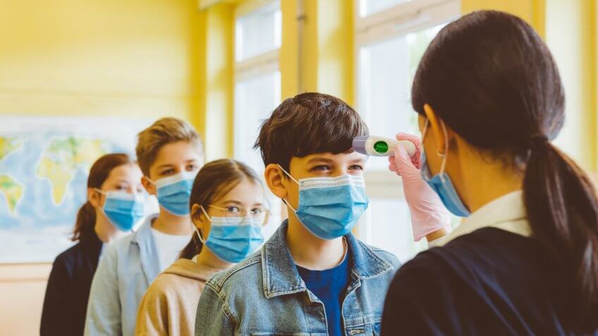 A teacher checks temperature of students at school.