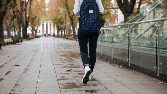 Back view of beautiful young woman with backpack walking in park.
