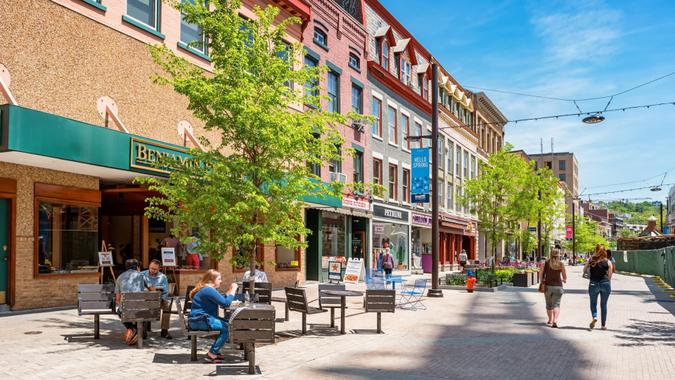 People have lunch and walk in a pedestrian area of downtown Ithaca, New York State, USA on a sunny day.