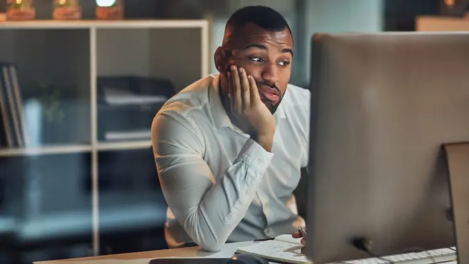 Shot of a young businessman looking bored while working at his desk during late night at work.