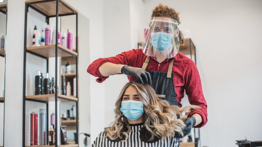 Young woman have hair cutting at hair stylist during pandemic isolation, they both wear protective equipment.