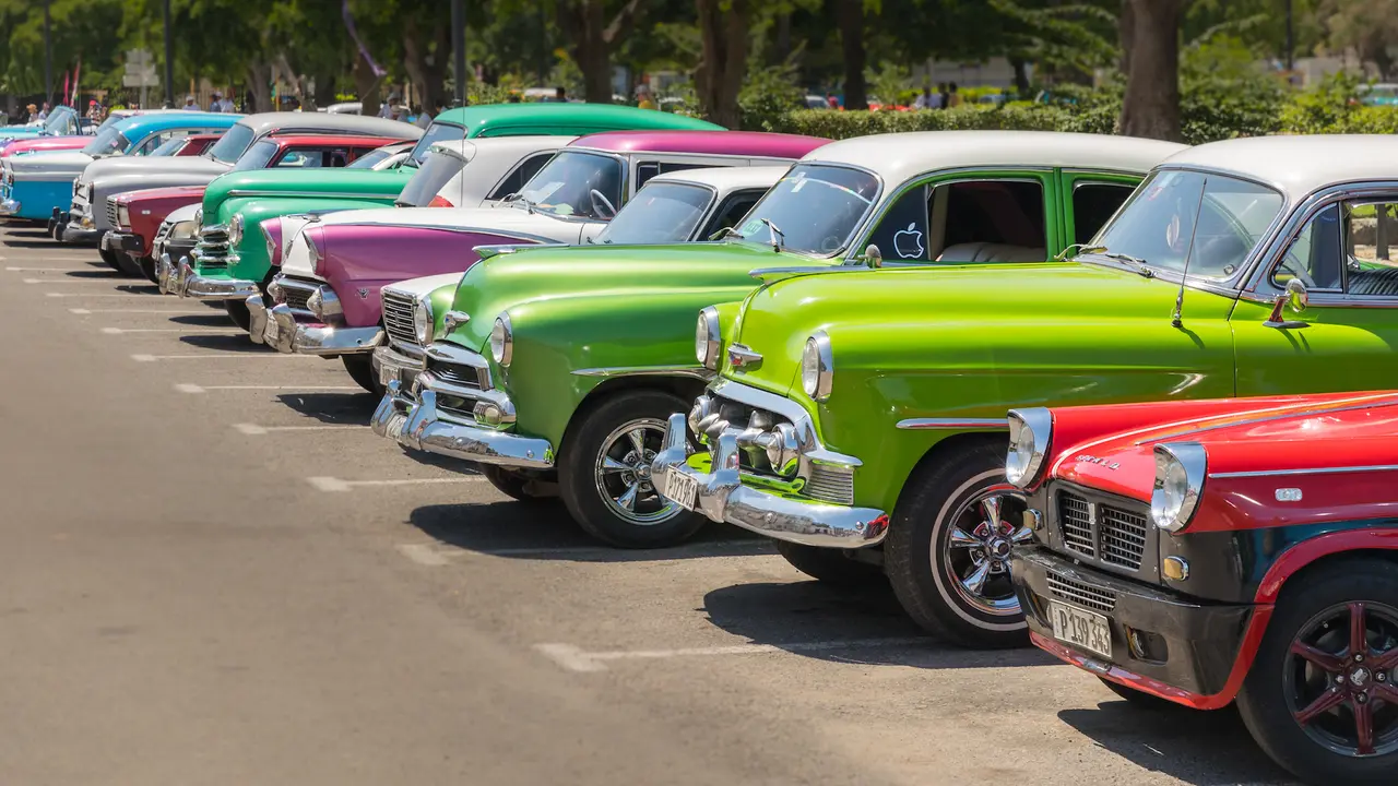 Havana, Cuba – July 23, 2018; A row of typically colorful Cuban vintage cars are lined up in a parking lot during the day.