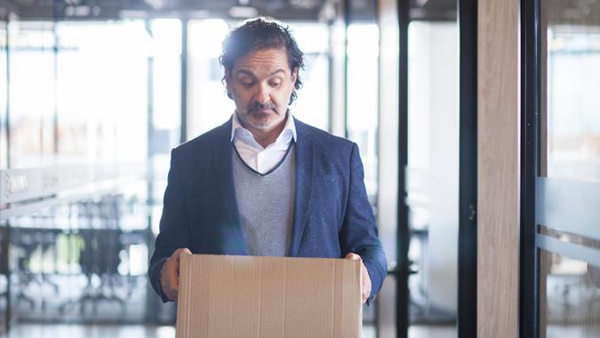 Latin executive man of approximately 50 years dressed in blue suit gray coat and white shirt walks through the corridors of the company where he works with a cardboard box where he carries his personal things in his hands which looks sadly since it was fired from his work half body picture.