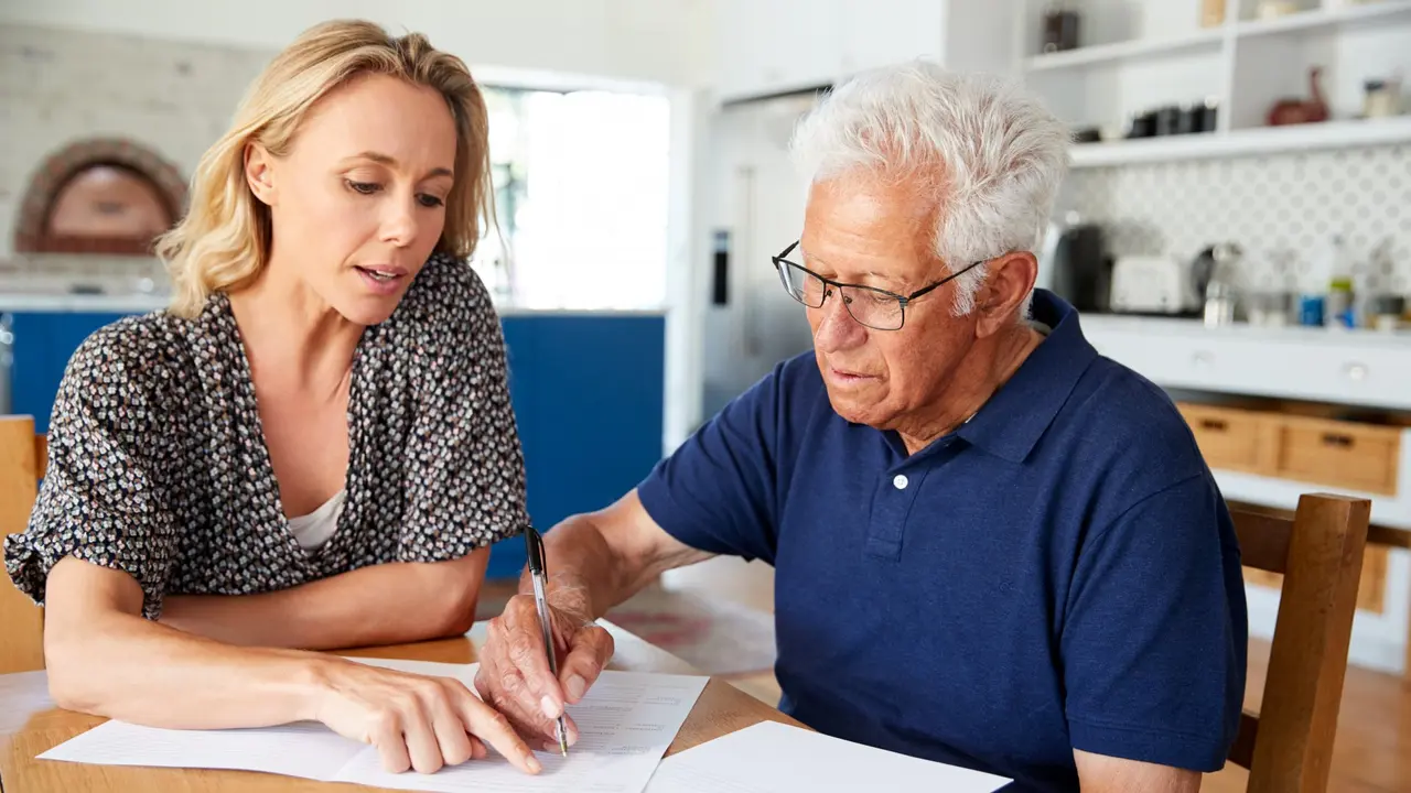 Woman Helping Senior Man To Complete Last Will And Testament At Home.