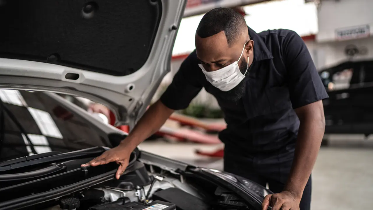 Auto mechanic man with face mask working at auto repair shop.