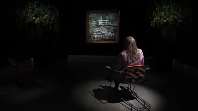 Mandatory Credit: Photo by Alastair Grant/AP/Shutterstock (10961697d)Member of staff poses in front of an artwork by Banksy entitled 'Show Me The Monet" at Sotheby's auction house in London, .