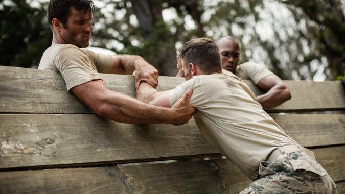 Soldiers helping man to climb wooden wall in boot camp