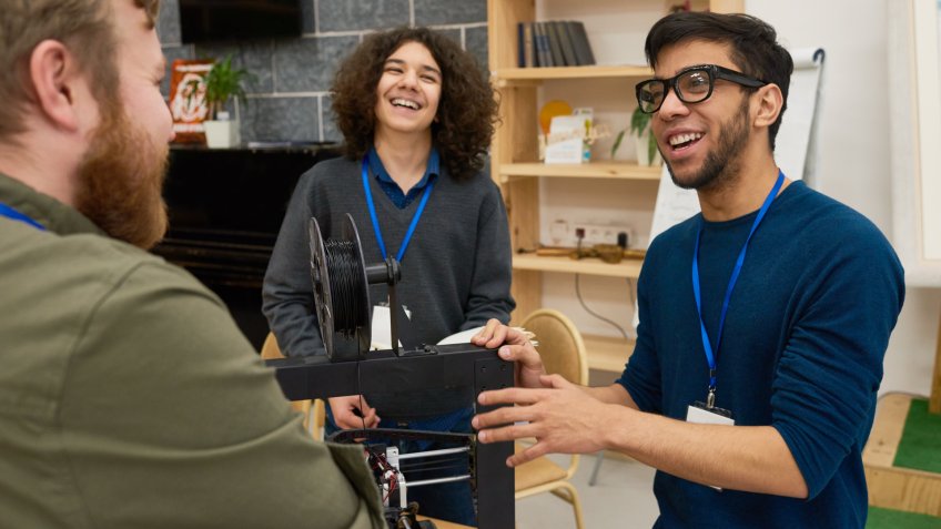 Cheerful young men discussing scientific project together, they standing near 3D printer.