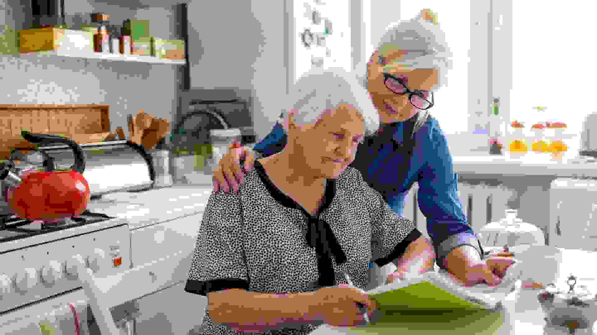 Mature woman helping elderly mother with paperwork.