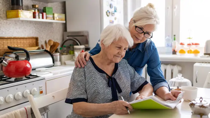 Mature woman helping elderly mother with paperwork.