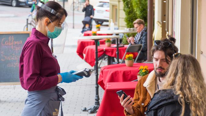 Waitress with a mask and clients at an outdoor bar, café or restaurant, reopen after quarantine restrictions.