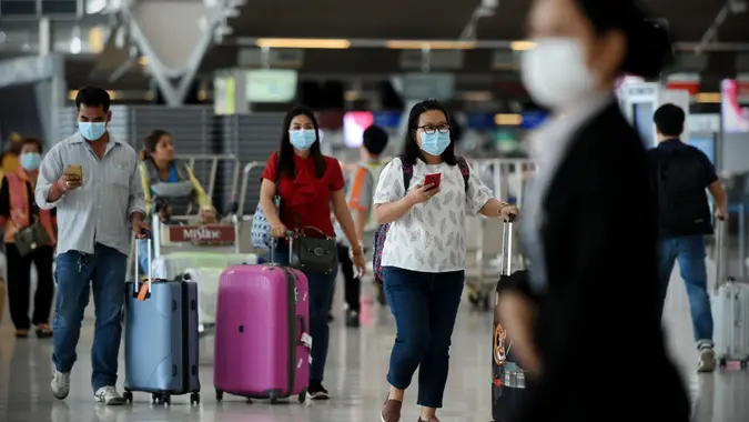 Bangkok, Thailand - February 18, 2020: Air travelers wearing masks walk through departures hall of Suvarnabhumi Airport.